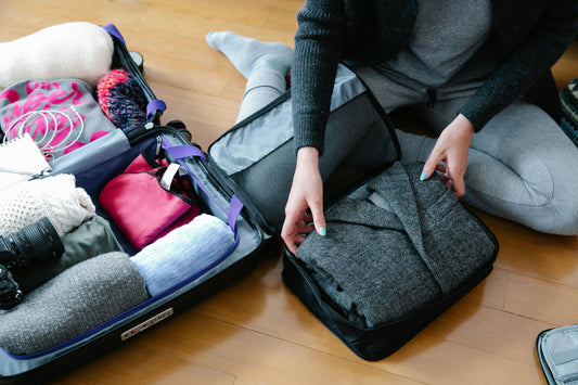 Person packing clothes into a bag next to an open suitcase.