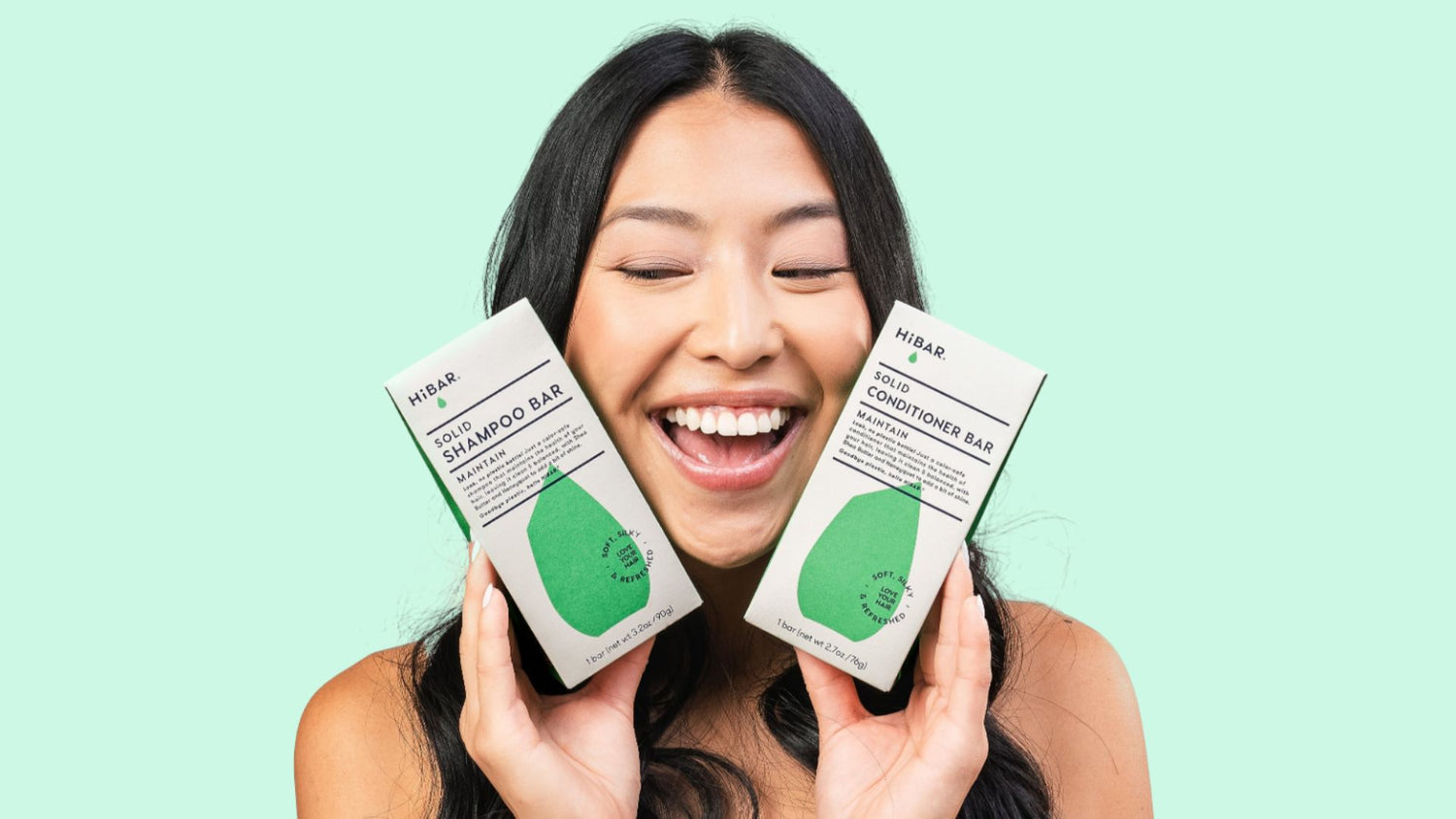 A woman with black hair holding two green haircare bars on a green background.