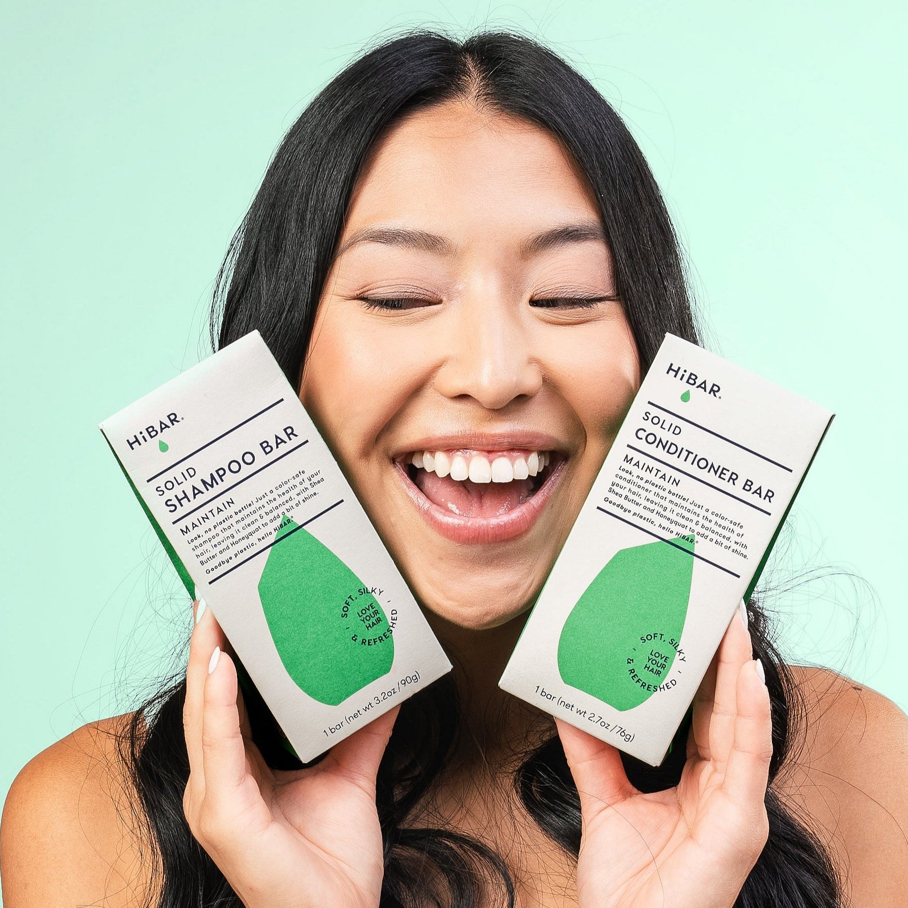 Model with black hair holding green Hibar shampoo and conditioner bars on a green background.