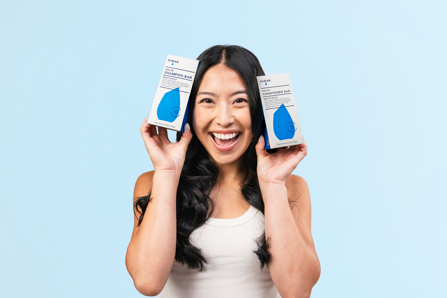 Long haired woman holding blue shampoo and conditioner bars on a blue background.
