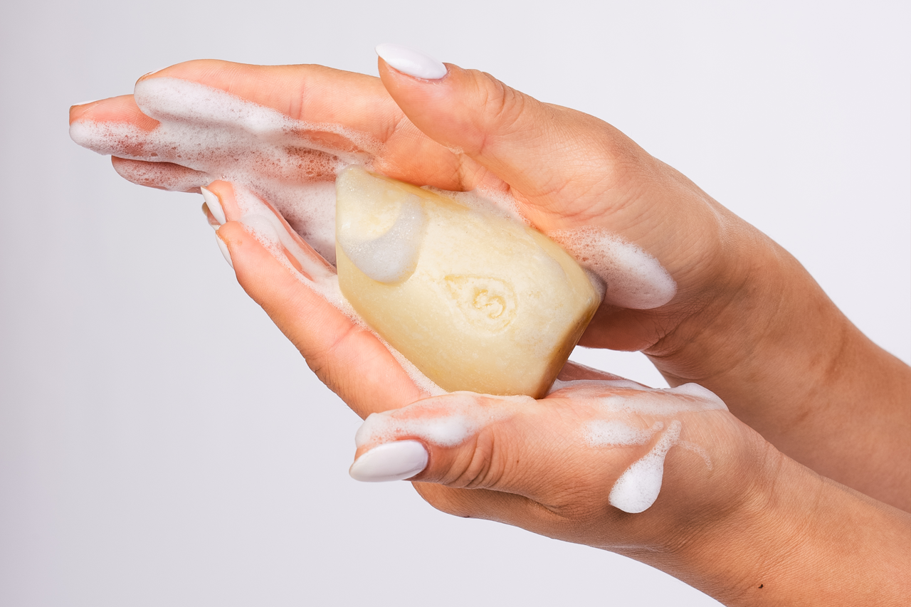 Two hands holding a yellow shampoo bar on a white background.