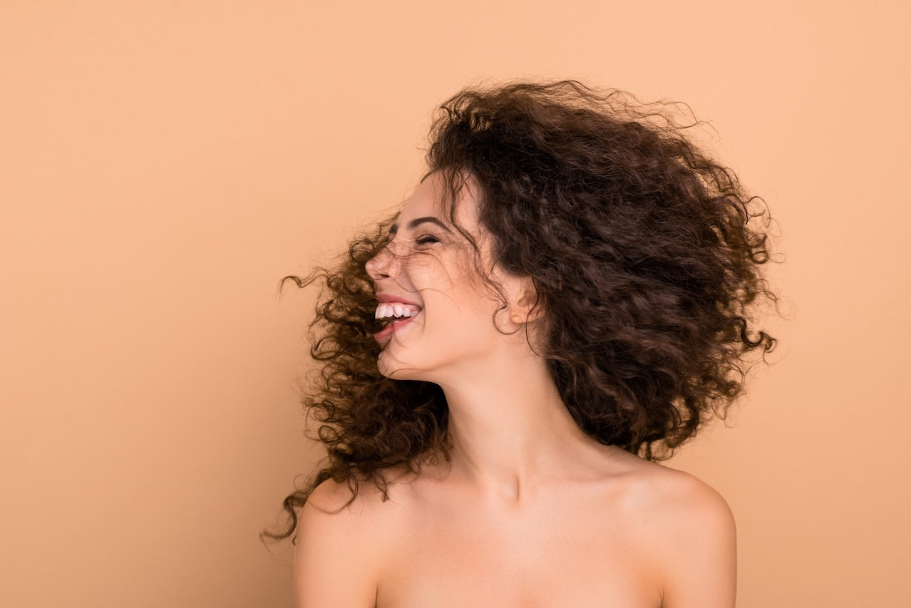 Model with curly hair smiling against a beige background.