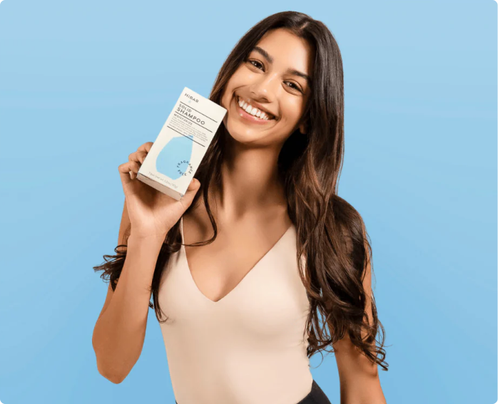 Smiling woman holding a Hibar solid shampoo bar on a blue background.