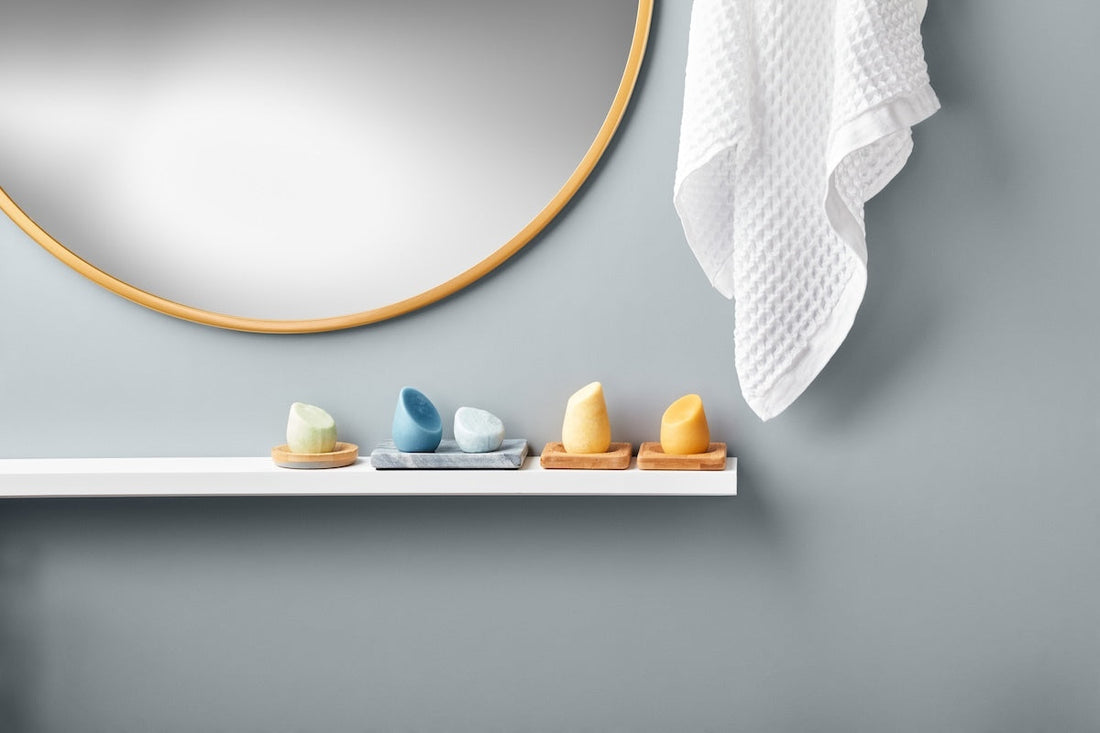 An image of a white shelf on a gray wall with a mirror above it, showing 5 shampoo bars.