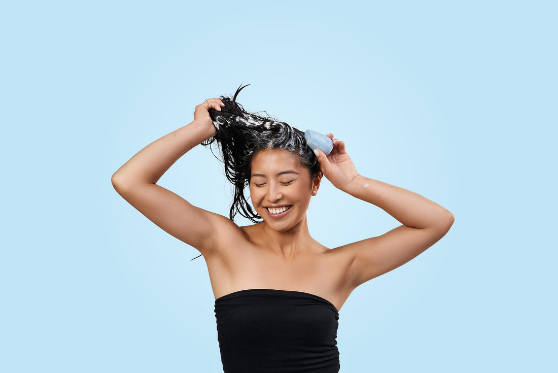 A woman with dark hair applying a blue shampoo bar on a blue background.