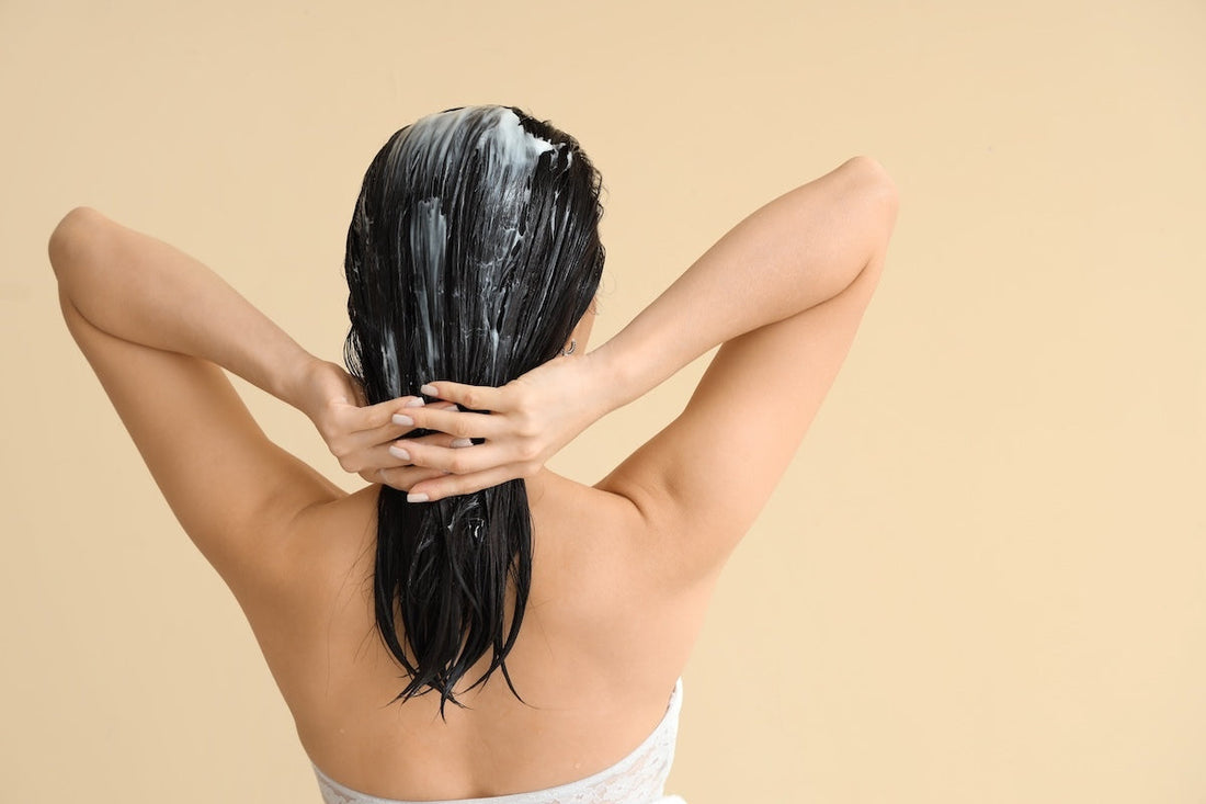 An image of a woman conditioning her hair in front of a light brown background.