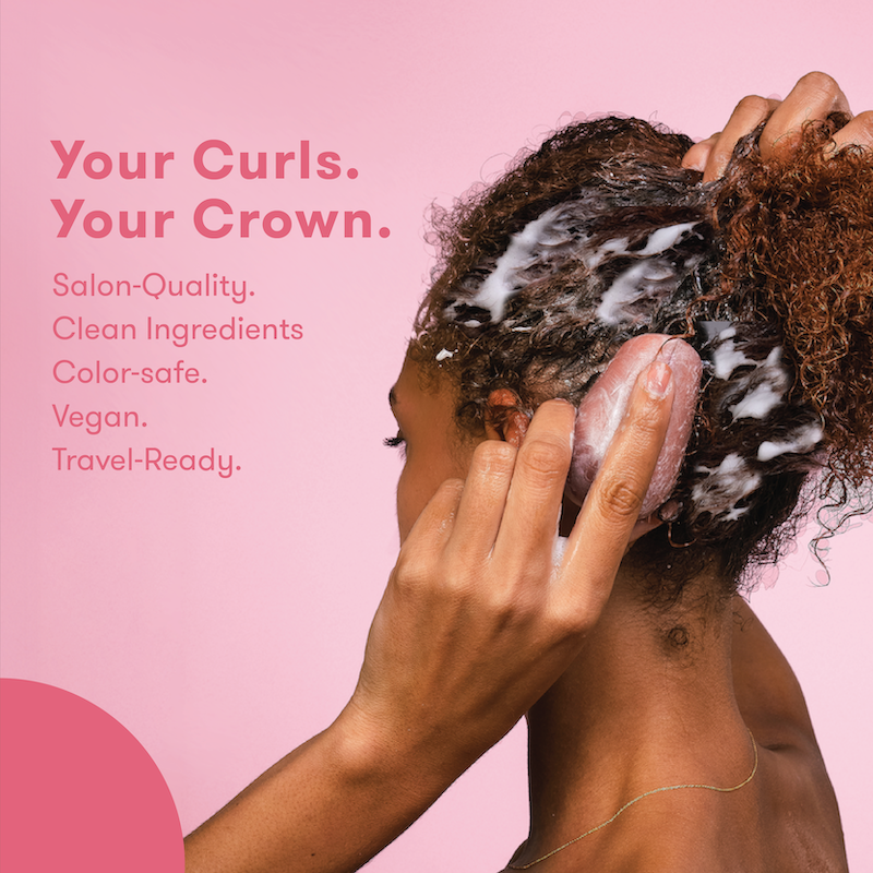 Picture of a woman with lathered hair, holding HiBAR shampoo bar against her head with text that reads: Your Curls. Your Crown. Salon Quality. Clean, Vegan Formula. Color-safe. Travel-Ready.