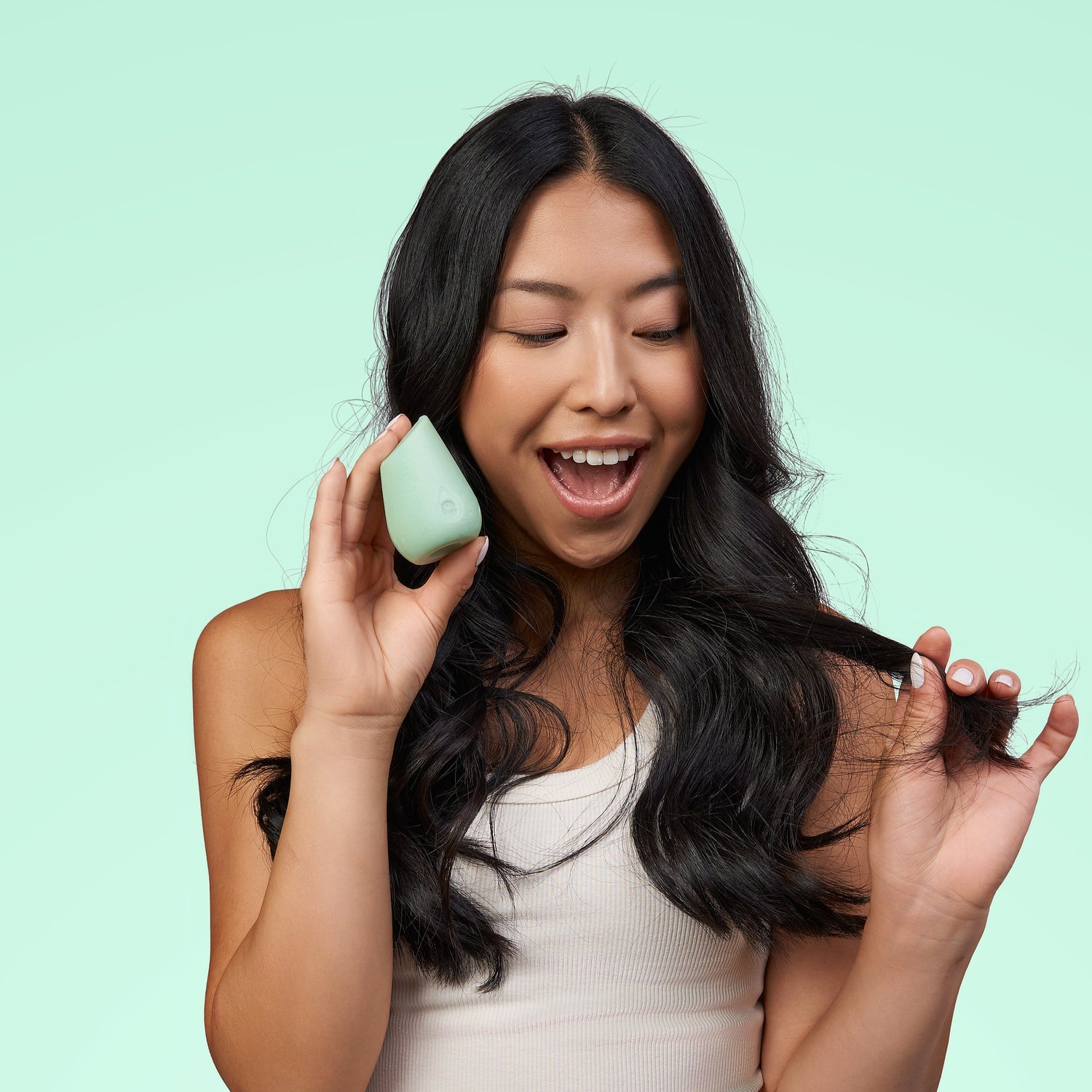 Model with dark wavy hair holding a green Hibar conditioner bar on a green background.