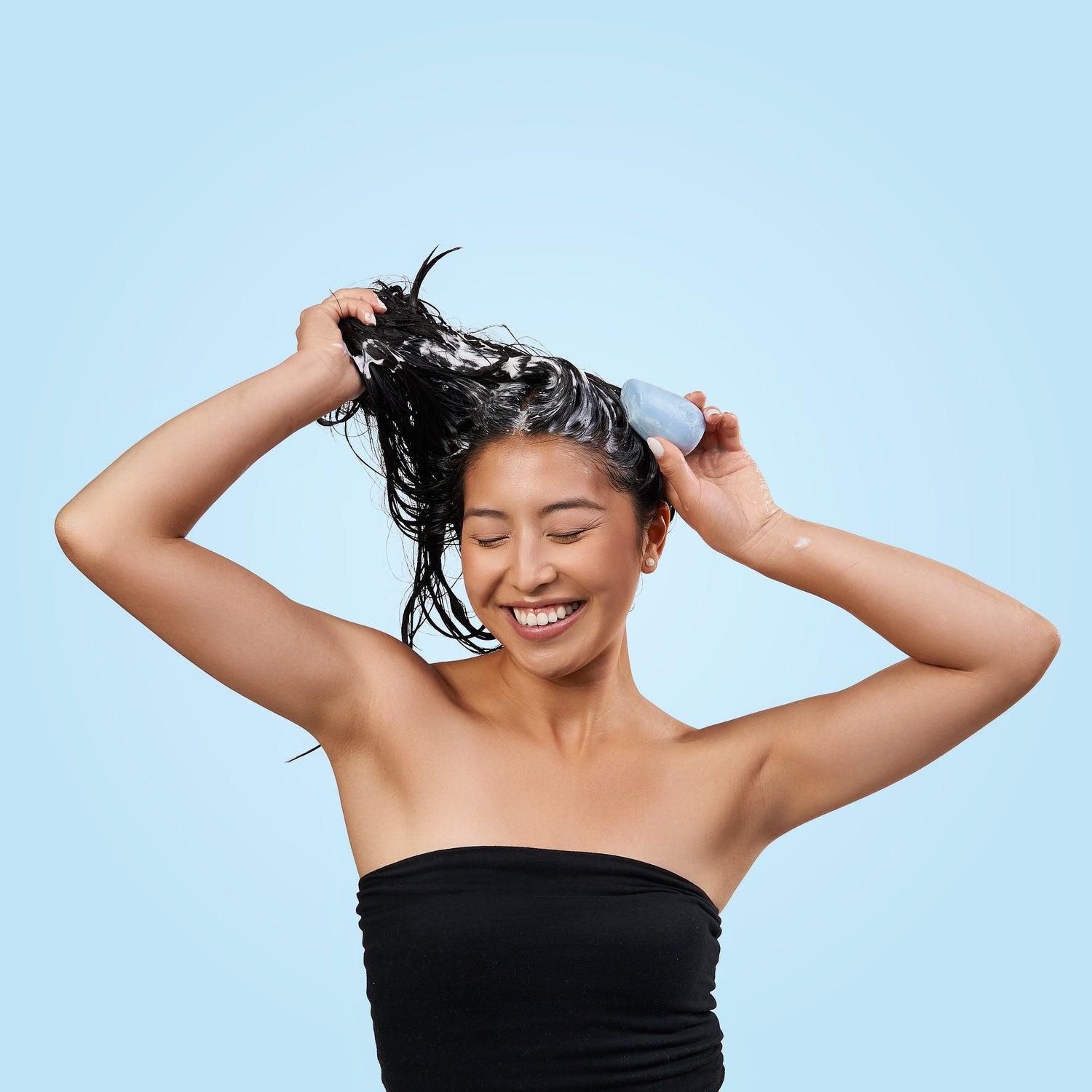 Woman with wet hair holding a blue shampoo bar on a blue background.