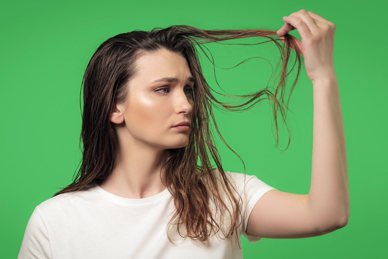 Woman looking at dry dark hair on a green background.