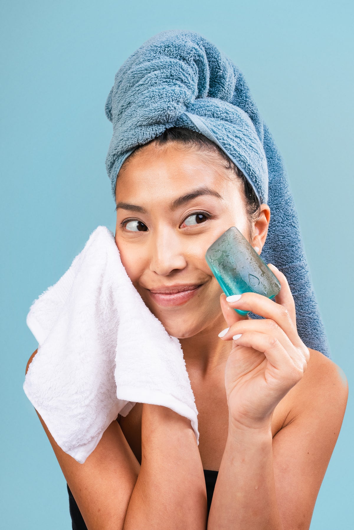 Female model with a blue hair towel holding a blue face wash bar against a blue background.