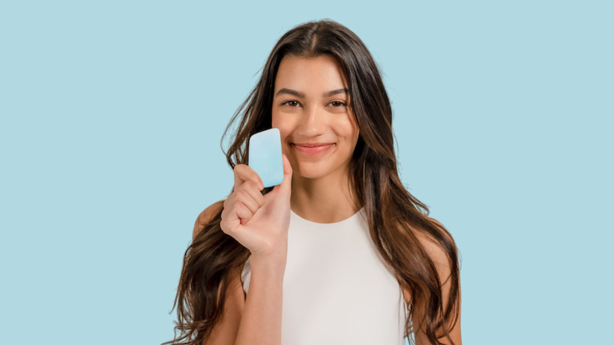 Woman with long brown hair holding a blue face wash bar against a blue background.